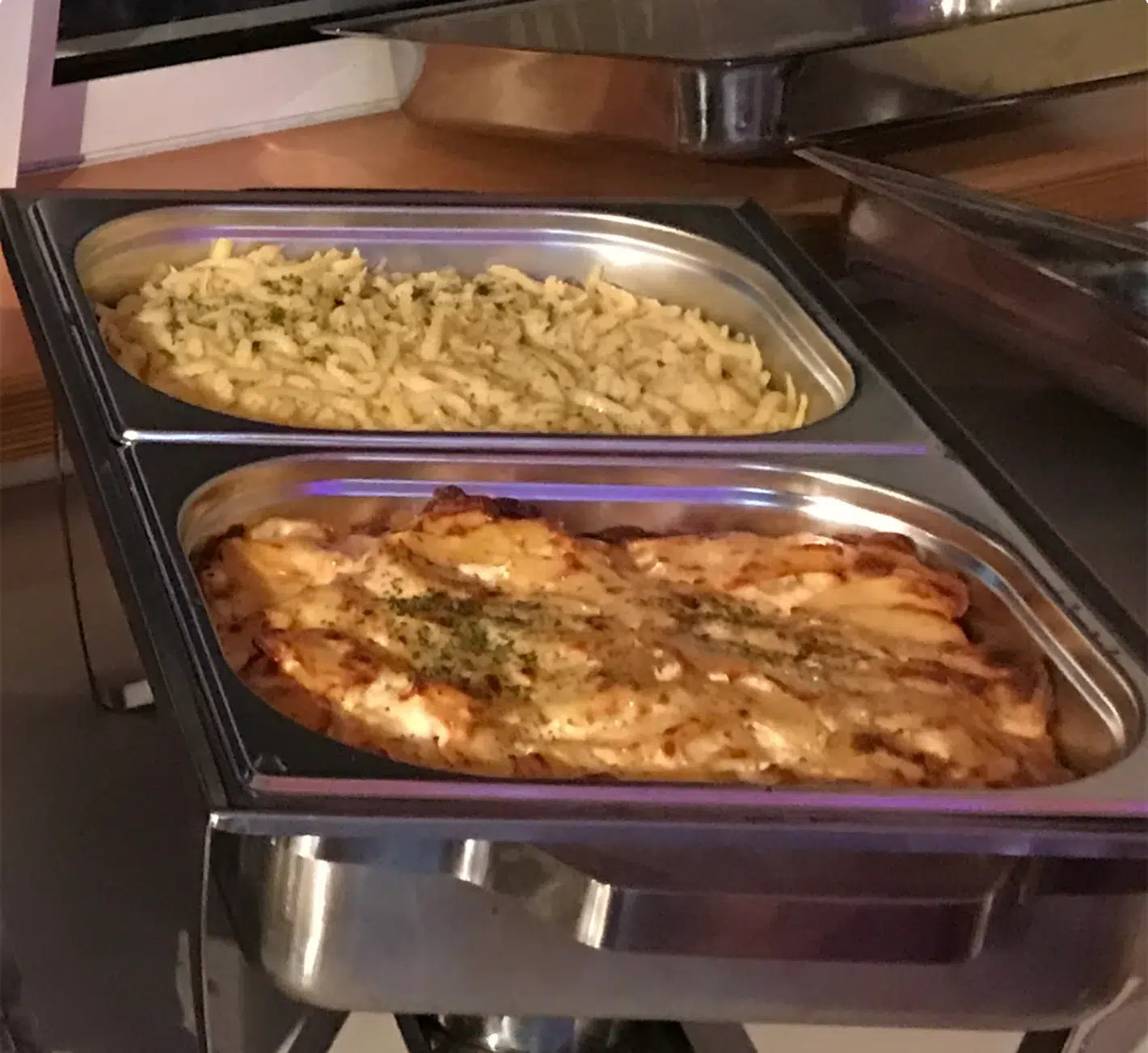 Buffet mit warmen Speisen, darunter Nudeln und ein Auflauf in Edelstahlbehältern – Evangelische Gesellschaft für Deutschland KdöR