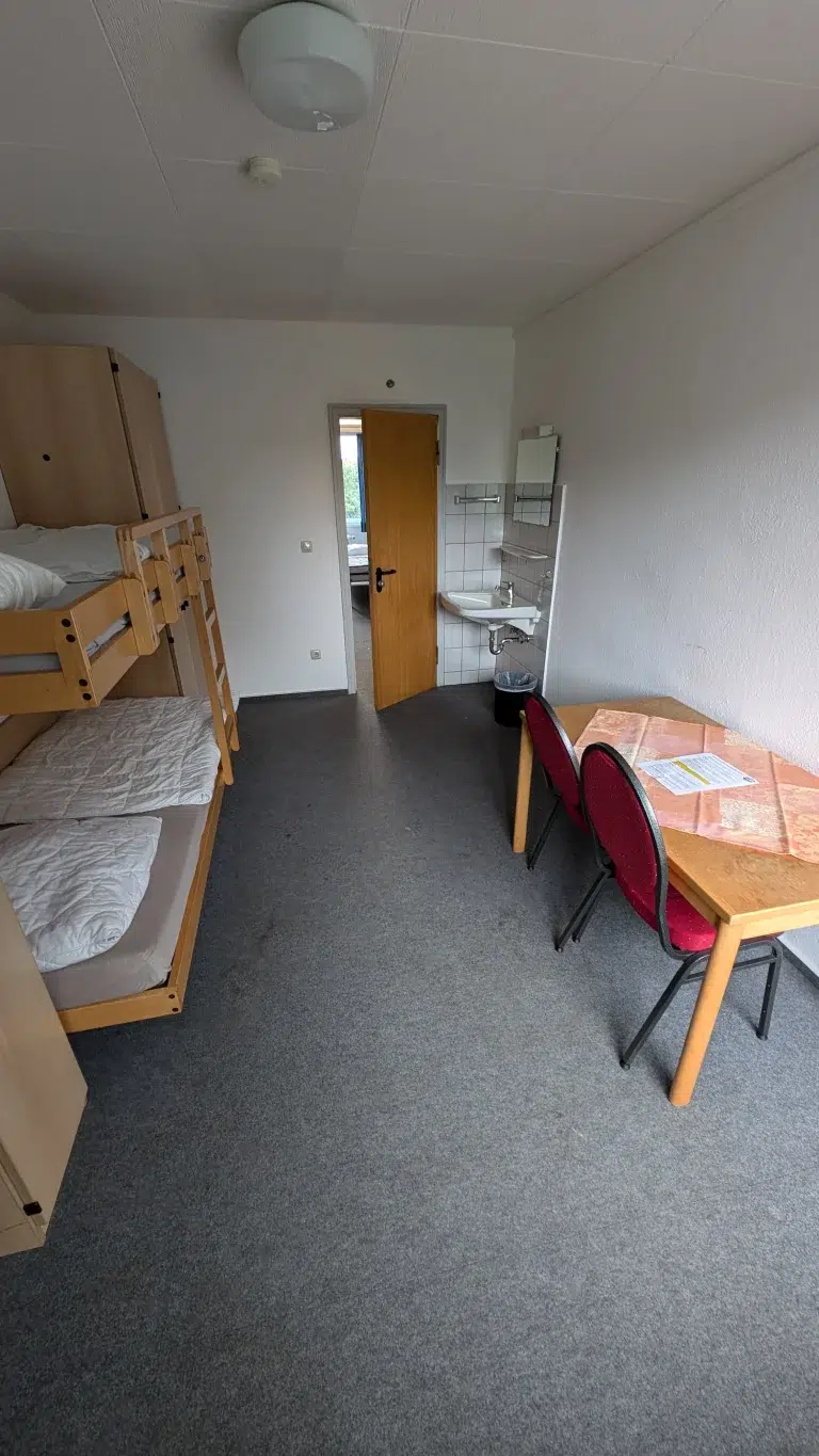 Kleines Zimmer mit Etagenbett, Tisch, Stühlen und Tür im Hintergrund – Evangelische Gesellschaft für Deutschland KdöR